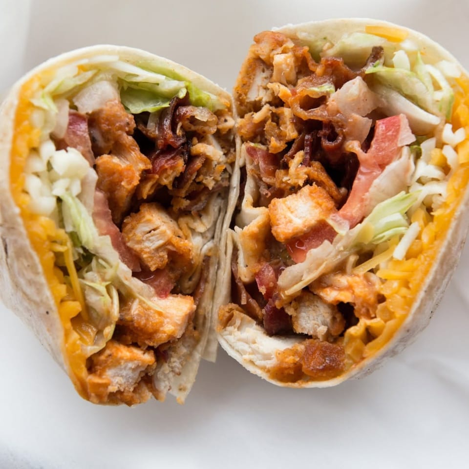 A Badda Bing's Italian Beef & Sausage wrap, cut in half, revealing chicken, bacon, lettuce, and cheese.